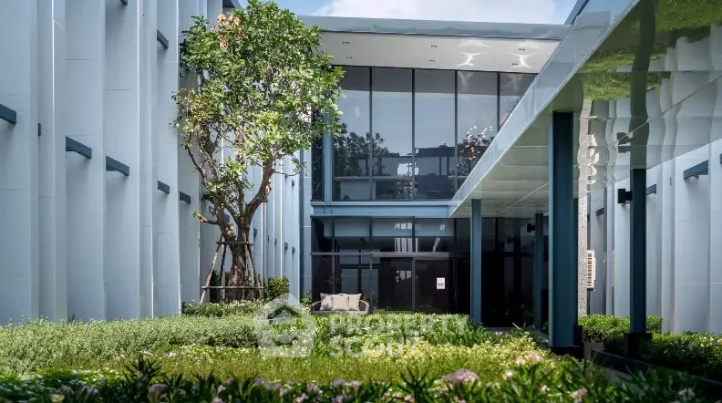 Modern building entrance with lush garden and glass facade, offering a serene and inviting atmosphere.