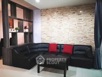Stylish living room with modern black leather sectional sofa and accent brick wall