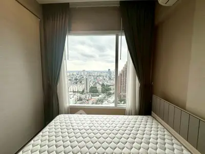 Modern bedroom with stunning city view from large window, featuring elegant curtains and a comfortable bed.