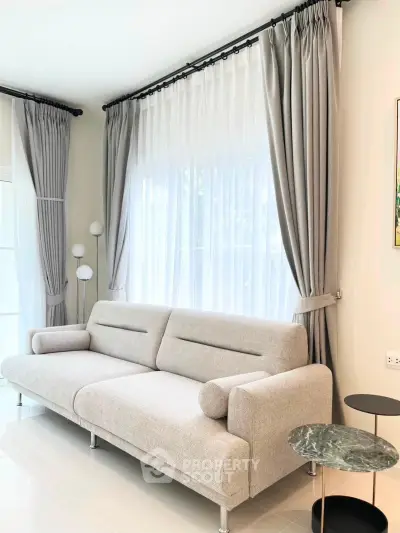 Elegant living room with modern sofa and floor-to-ceiling windows, featuring stylish curtains and a chic side table.