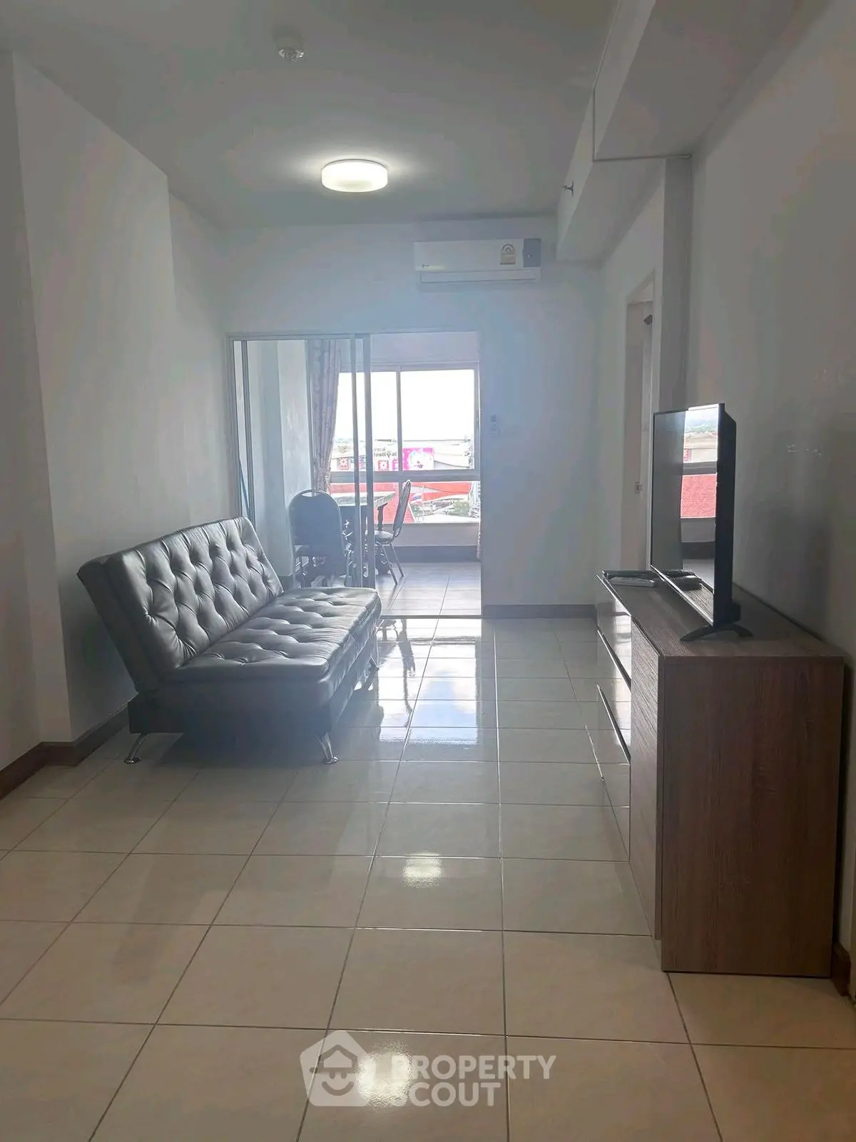 Modern living room with sleek sofa and TV, leading to a bright balcony view.