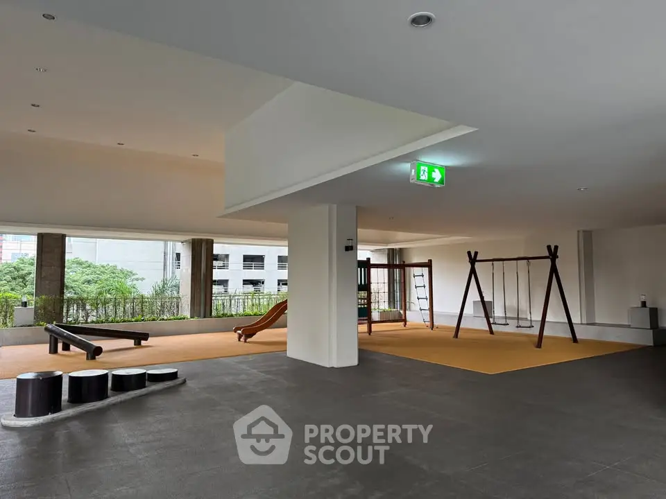 Spacious indoor playground area in modern residential building with swings and slide.