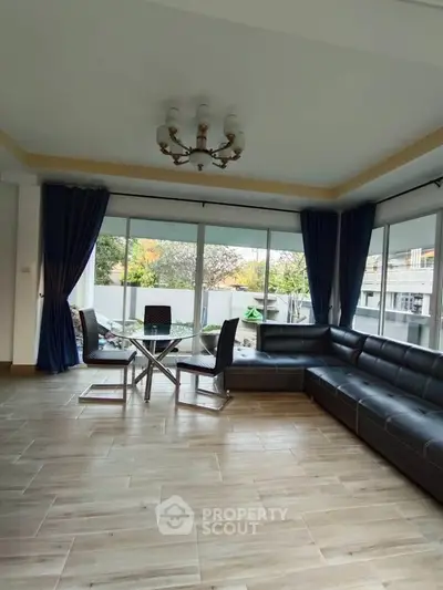 Spacious living room with modern furniture and large windows offering natural light and garden view.