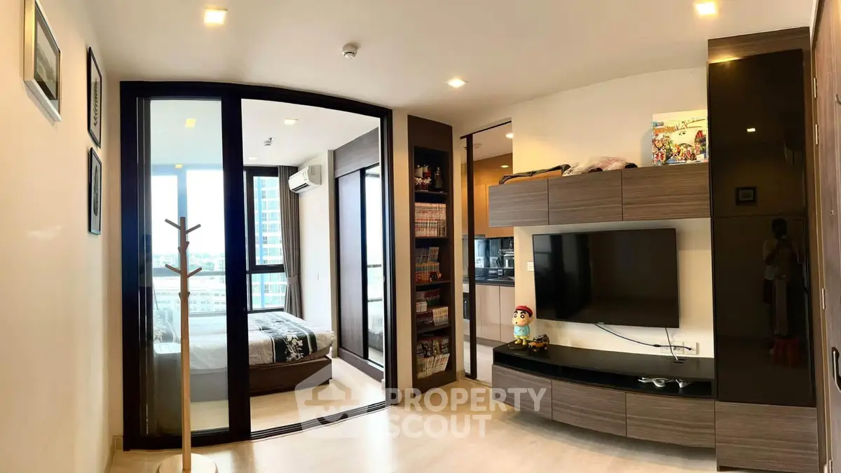 Modern living room with sleek TV unit and glass partition leading to bedroom with city view.