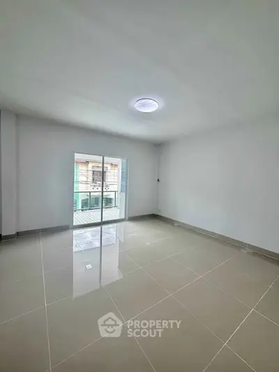 Spacious empty room with glossy tiled floor and sliding glass doors leading to balcony.