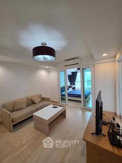 Modern living room with cozy sofa and TV, leading to a bright bedroom with large windows.