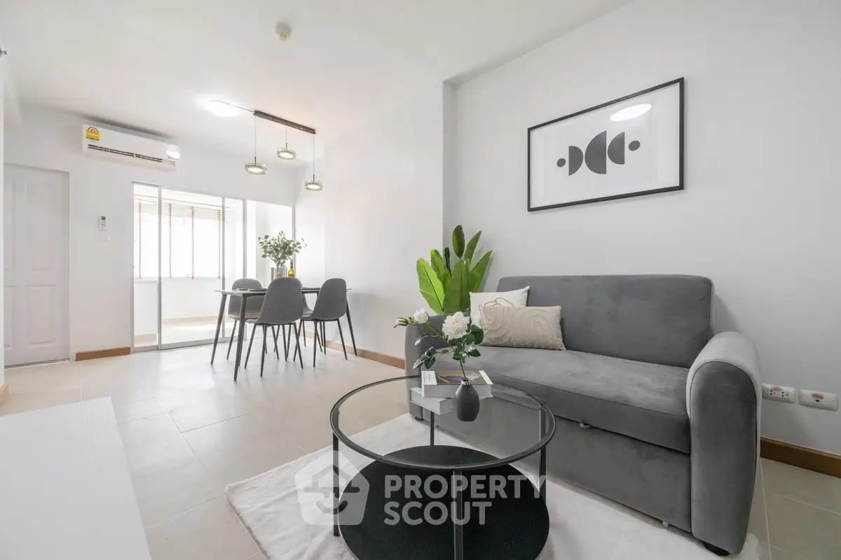 Modern living room with stylish decor and open dining area, featuring a cozy gray sofa and elegant lighting.