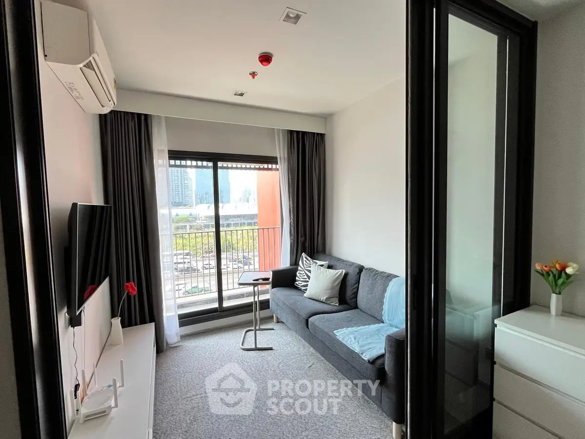 Modern living room with plush sofa, sleek design, and access to a sunlit balcony offering an urban view, perfect for relaxation and entertainment.