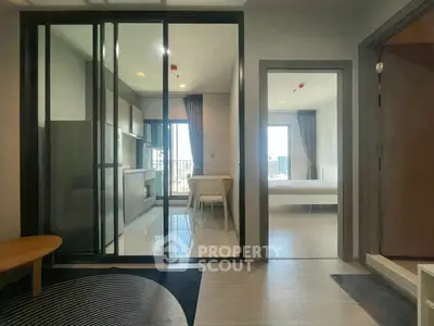 Modern apartment interior with open kitchen and bedroom view, featuring sleek glass partition and stylish decor.