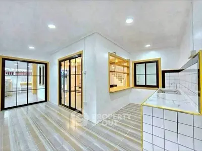 Modern open-layout kitchen with sleek design and spacious dining area, featuring large windows and stylish flooring.