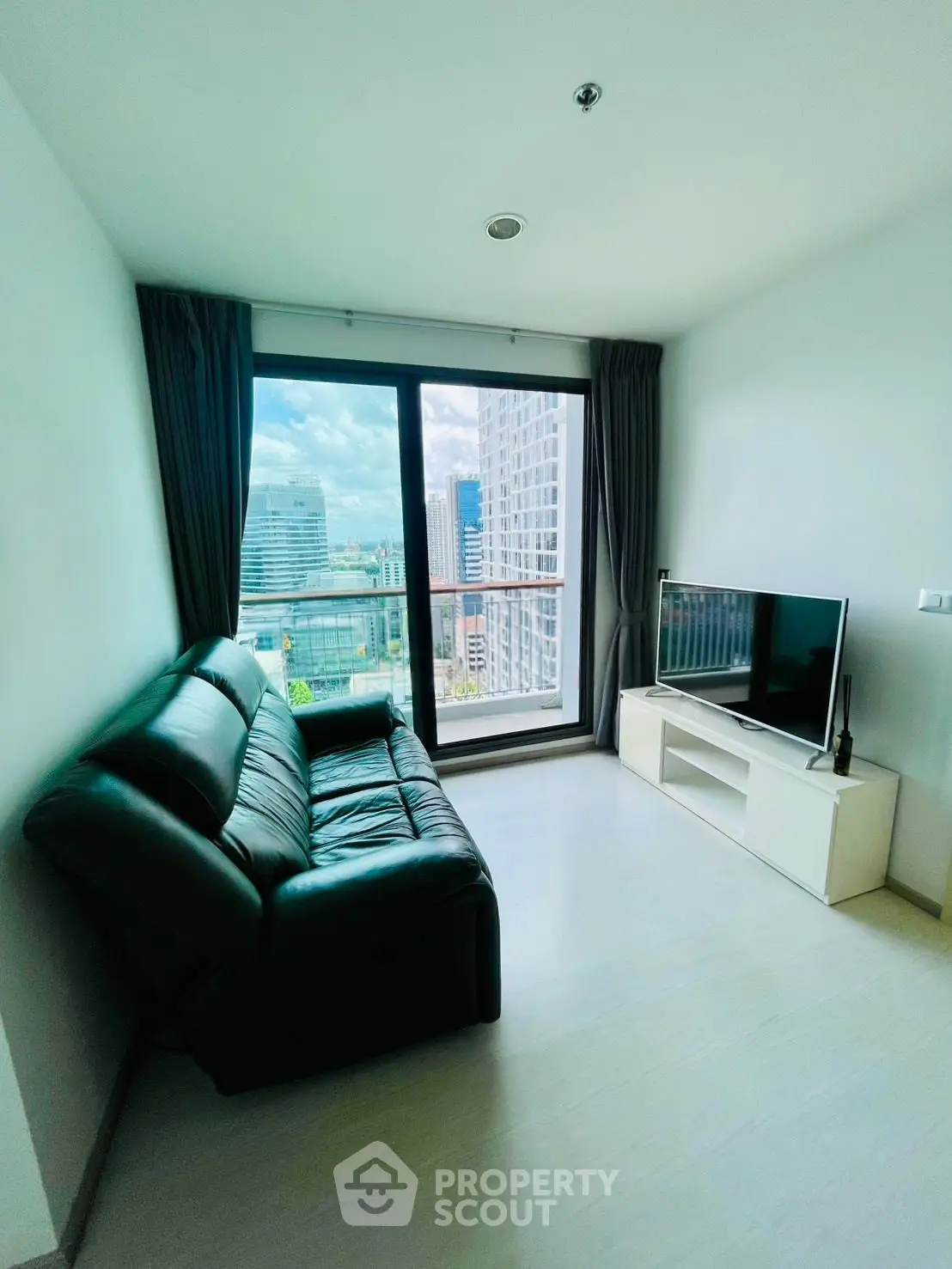 Modern living room with city view, featuring sleek black sofa and large window for natural light.