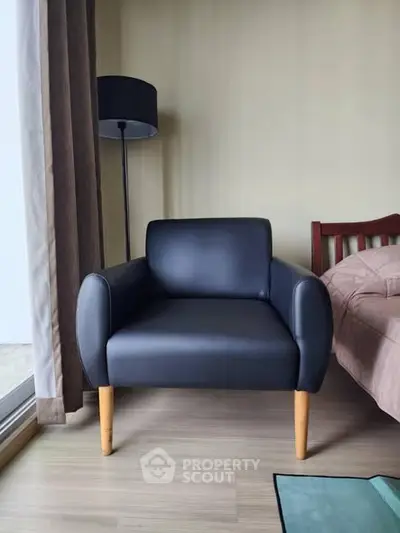 Modern bedroom with sleek black armchair and cozy bed near large window.