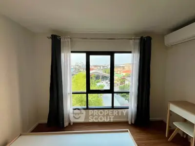 Bright bedroom with large window offering scenic city view, featuring modern air conditioning and minimalist decor.