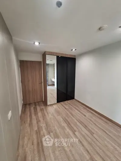 Spacious empty bedroom with wooden flooring and mirrored wardrobe