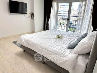 Spacious bedroom with balcony and city view, featuring modern decor and wall-mounted TV.
