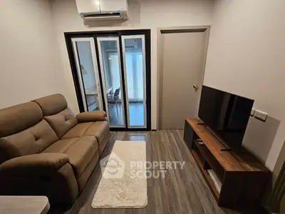 Modern living room with cozy sofa and flat-screen TV, featuring sleek flooring and air conditioning.