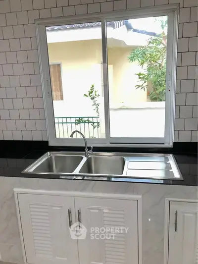 Modern kitchen with sleek stainless steel sink and large window offering natural light.
