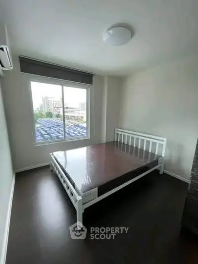 Spacious bedroom with large window offering city views, featuring a modern bed and sleek flooring.