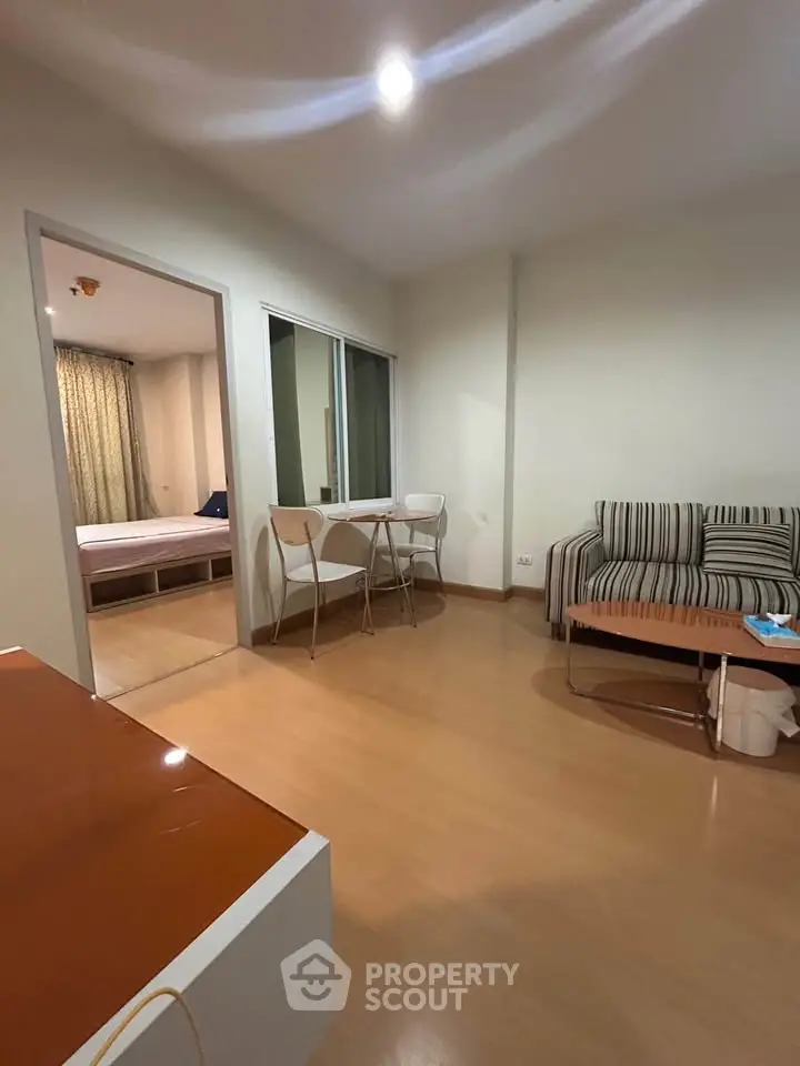 Cozy living room with striped sofa and dining area, adjacent to a bedroom with soft lighting.