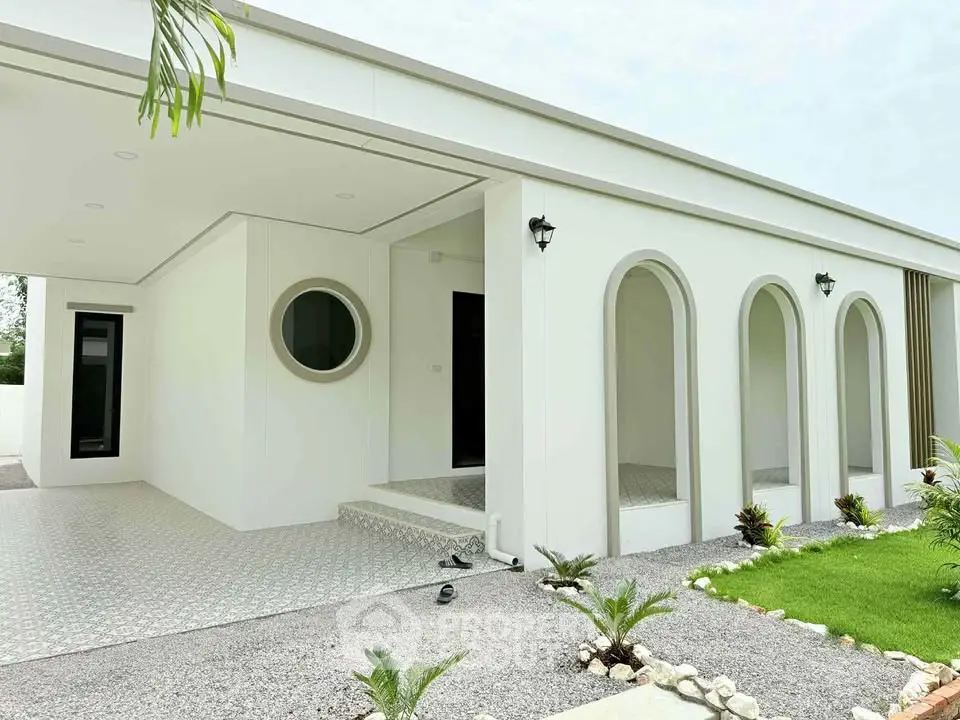 Modern minimalist white house exterior with unique circular window and arched entryways.
