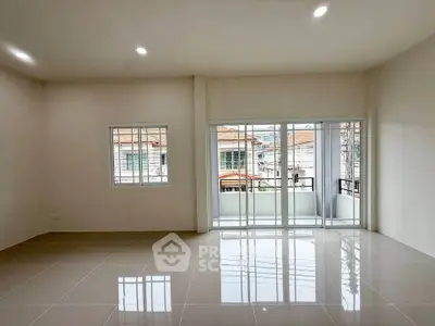 Spacious living room with large windows and balcony access, offering ample natural light and modern tiled flooring.