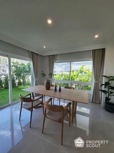 Elegant dining area with large windows and garden view, featuring modern wooden table and chairs.