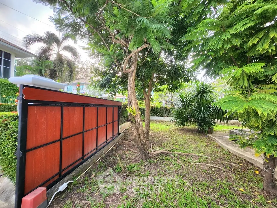 Lush garden with trees and a modern red fence in a residential area.