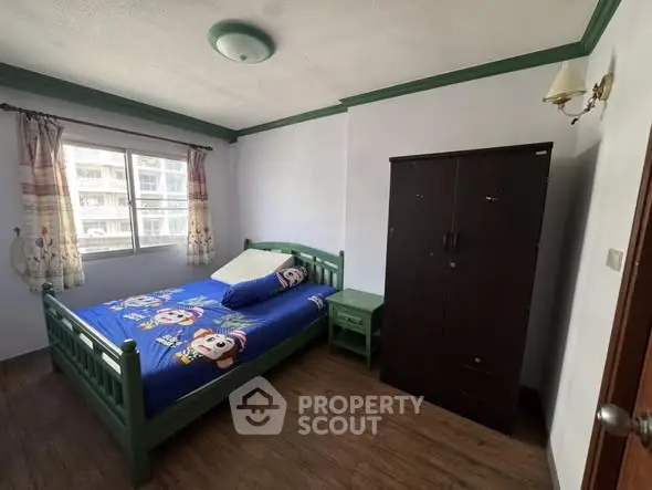 Cozy bedroom with green bed frame and wardrobe, featuring a window view.