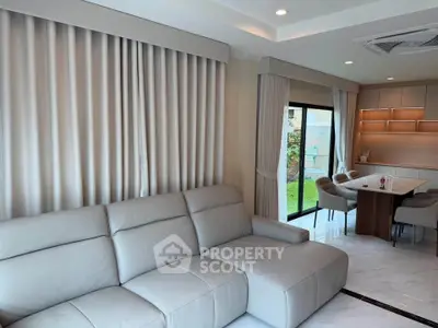 Modern living room with elegant sofa and dining area, featuring large windows and stylish curtains.