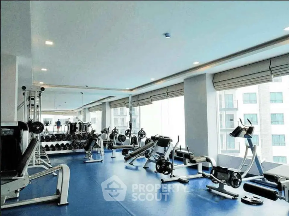 Spacious gym with modern equipment and large windows in luxury apartment building.