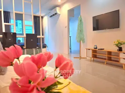 Modern living room with stylish decor, wall-mounted TV, and vibrant pink flowers enhancing the ambiance.