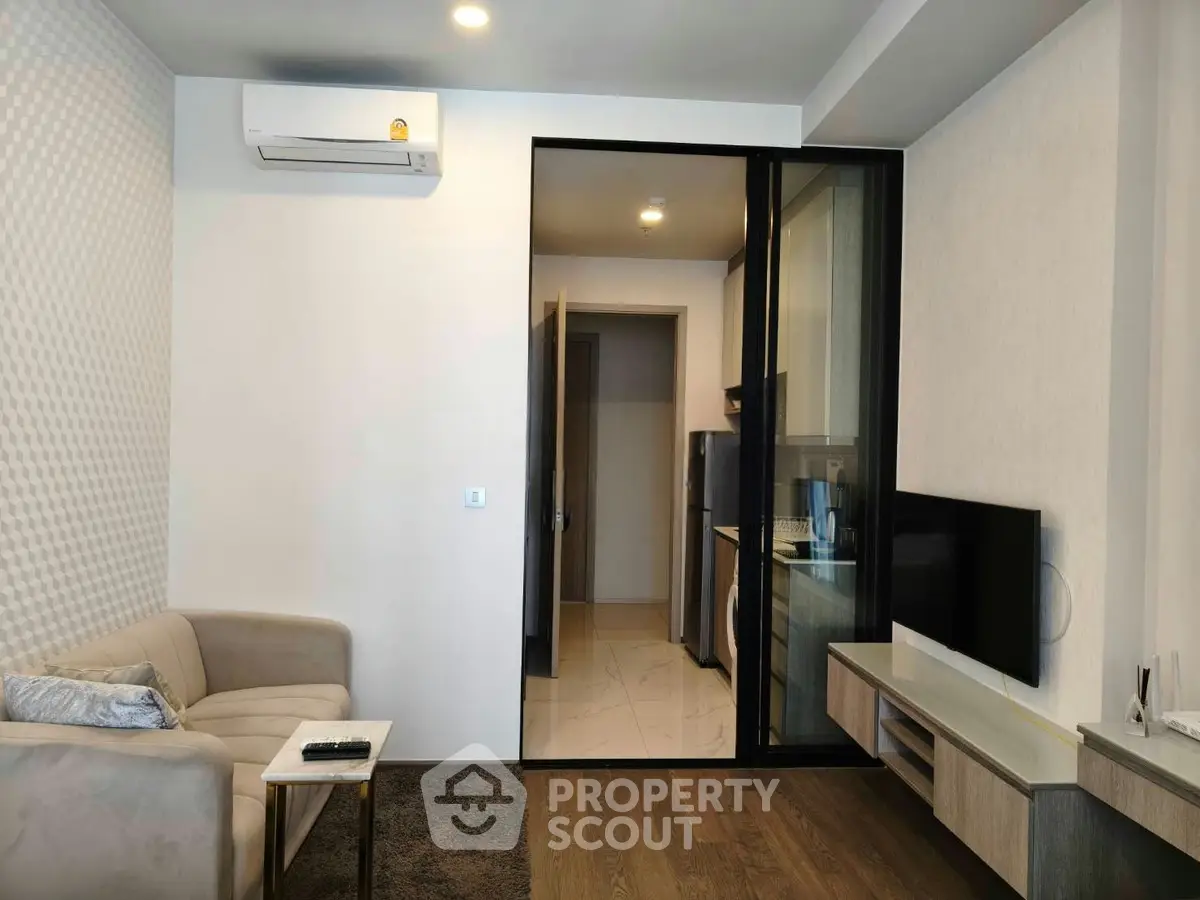 Modern living room with air conditioning and open kitchen layout, featuring sleek furniture and wooden flooring.