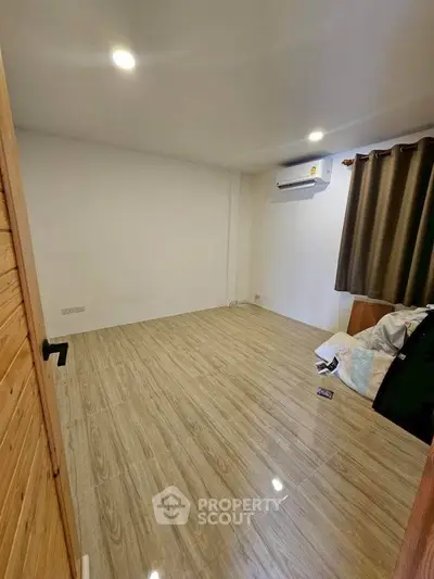 Spacious empty room with wooden flooring and air conditioning, ready for customization.