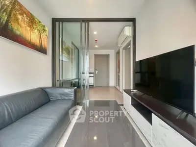 Modern living room with sleek furniture and large TV, featuring a glass partition and contemporary decor.