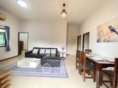 Spacious living room with modern decor and dining area, featuring a comfortable black sofa and elegant lighting.