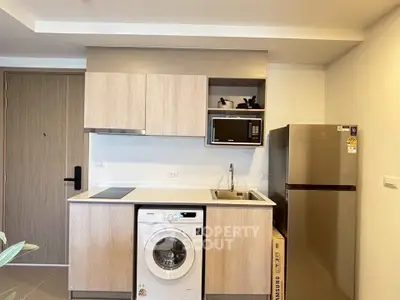 Modern kitchen with washing machine, microwave, and fridge in compact layout.