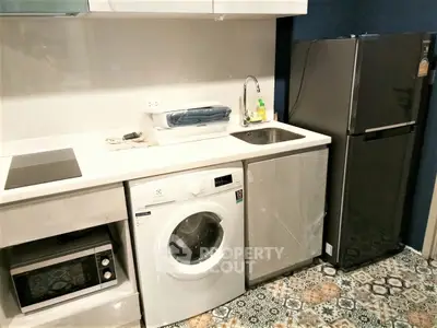 Modern kitchen with washing machine, fridge, and microwave in compact layout.
