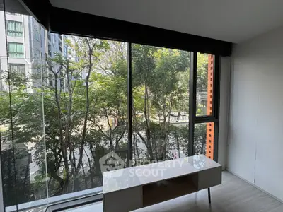 Modern apartment with large windows offering a serene view of lush trees and urban surroundings.
