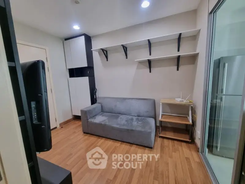 Modern living room with sleek sofa and open shelving, adjacent to a glass door leading to the kitchen.