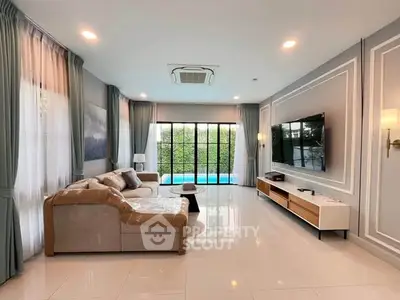 Spacious living room with modern decor and pool view, featuring a large TV and comfortable seating.