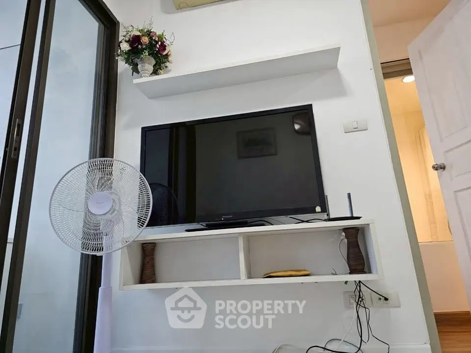 Modern living room with TV, fan, and decorative shelf in a cozy apartment.