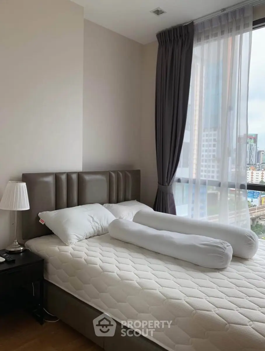 Modern bedroom with city view, featuring a stylish bed and elegant curtains.