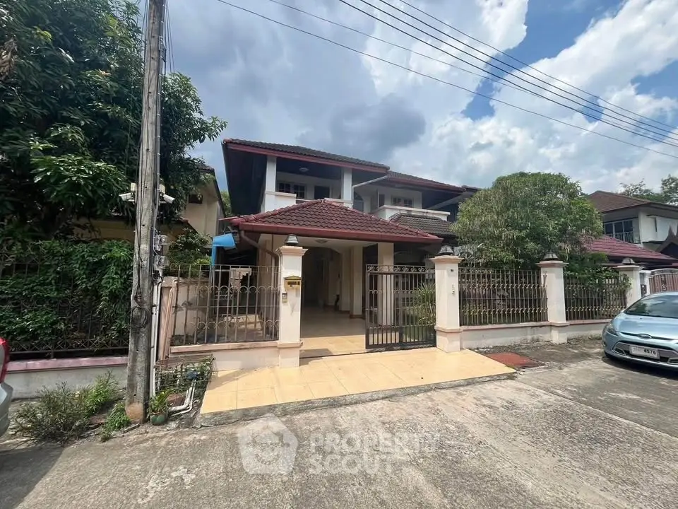 Charming two-story house with red roof and gated entrance in a serene neighborhood.