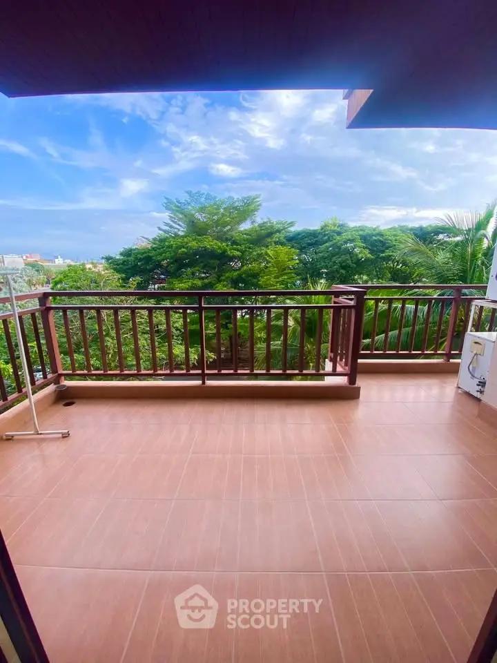 Spacious balcony with scenic green view and wooden railing, perfect for relaxation.