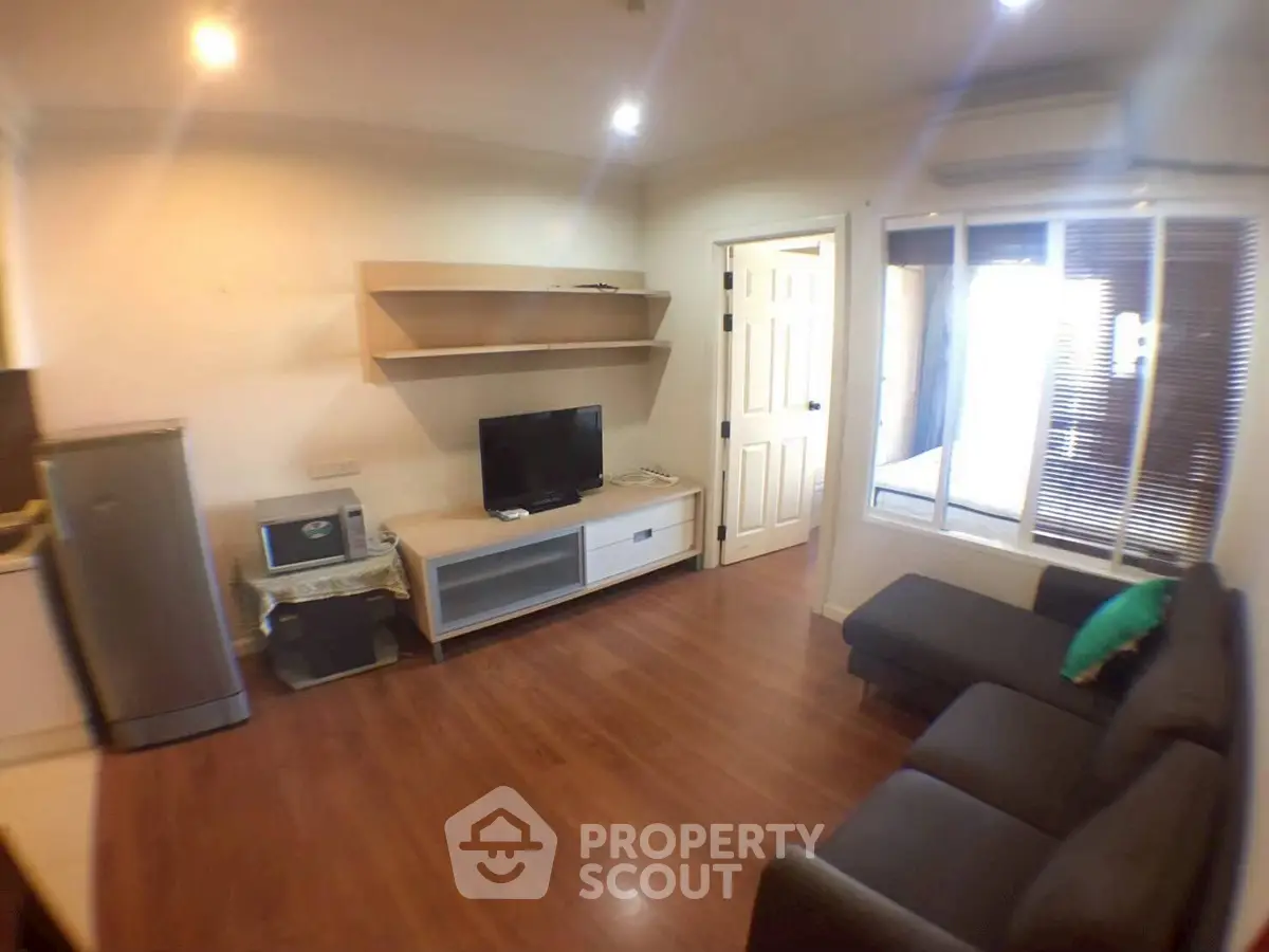 Cozy living room with modern furniture and wooden flooring, featuring a TV and ample natural light.