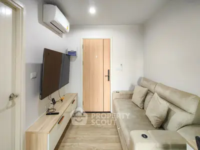 Modern living room with beige sofa, wall-mounted TV, and wooden flooring.