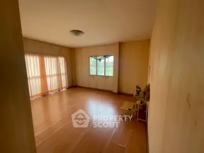 Spacious living room with large windows allowing ample natural light, featuring warm wooden flooring and a neutral color palette.