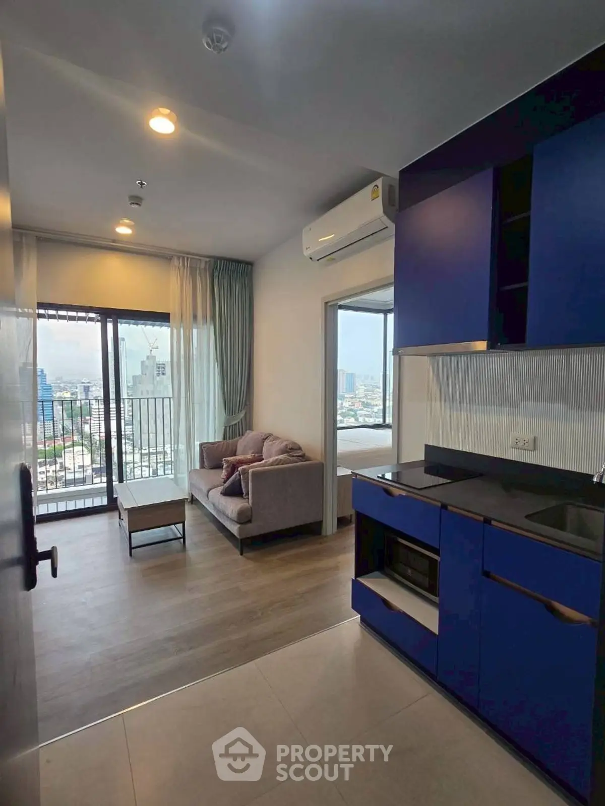 Modern apartment with open living area and city view, featuring sleek blue kitchen cabinets.