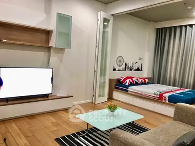 Modern living room with stylish decor and cozy bed area, featuring a sleek TV and wooden flooring.