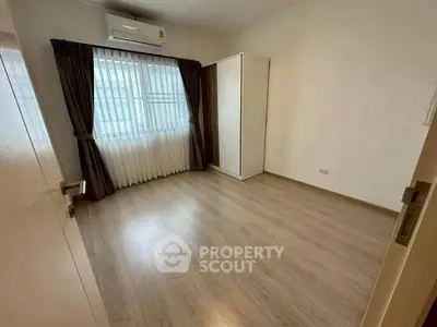Spacious empty bedroom with wooden flooring and large window, perfect for customization.